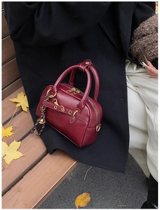 Détail d'un sac Boston vintage bordeaux en cuir sur un banc avec des feuilles d'érable d'automne