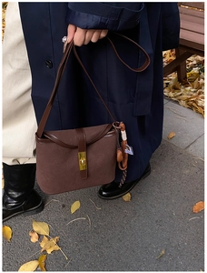 Close-up of vintage brown suede crossbody bag with gold buckle and tassel detail