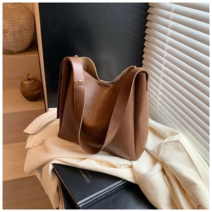 Detail of a brown leather bucket bag with wide shoulder strap in a minimalist style