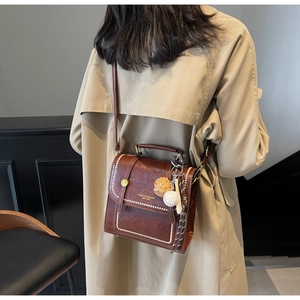 Close-up of vintage brown leather crossbody bag with white stitching and stylish charms