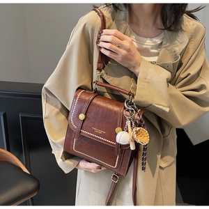 Close-up of caramel leather crossbody bag featuring gold studs and a baseball keychain