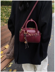 Détail macro du sac Boston en cuir bordeaux avec ferrures dorées et pendentif tissé