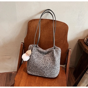 Détail du sac cabas en maille grise avec un charmant pendentif sur une chaise en bois