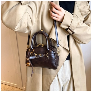 Détail d'un mini sac Boston marron foncé avec zip doré et pendentif pompon sur un mannequin