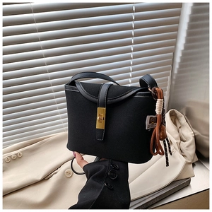 Detail of a matte black bucket bag with a gold twist lock and a woven tassel charm