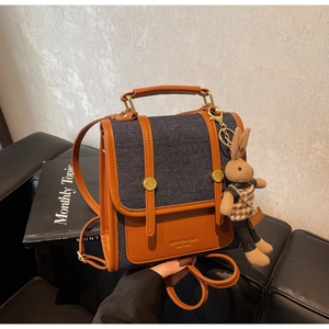 Detail of contrast stitch denim and brown leather backpack with cute rabbit charm