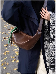Close-up of dark brown leather croissant bag with stylish woven rope pendant detail