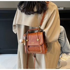 Close-up of vintage brown leather bag with white contrast stitching and baseball charm