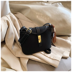 Detail of black matte shoulder bag featuring gold hardware and decorative woven charm