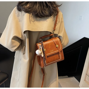 Detail of vintage brown leather satchel with gold hardware and baseball charm on coat