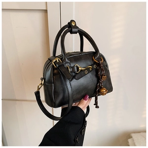 Détail d'un sac Boston rétro noir avec clochettes dorées et texture cuir poli chic