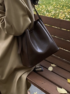 Minimalist large brown leather tote bag carried by a model in a scenic autumn park setting
