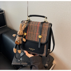 Close-up of retro plaid fabric with black leather stitching and cute bunny plush charm