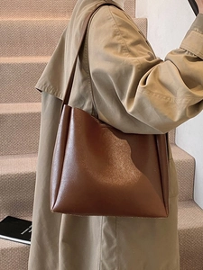 Minimalist large brown leather tote bag for women worn over shoulder with a trench coat