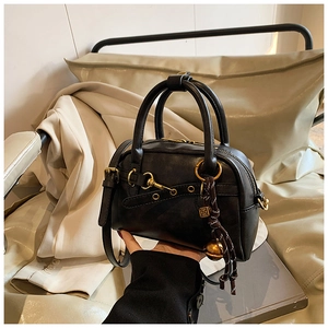Détail du sac Boston en similicuir noir avec ferrures dorées et breloque cloche