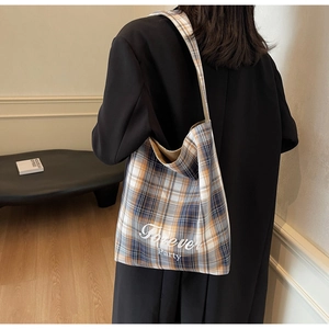 Détail du sac fourre-tout en toile à carreaux bleus et marrons porté à l'épaule