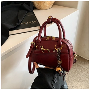 Détail du sac Boston bordeaux avec fermeture éclair dorée et breloque clochette