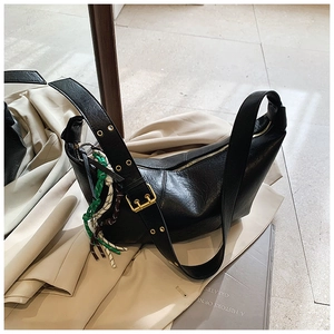 Detail of black crescent shoulder bag featuring textured leather and woven pendant