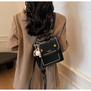 Detail of a black leather handbag with gold studs and sports charm worn over a blazer