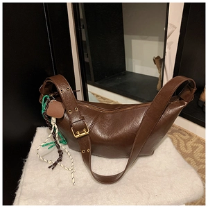 Detail of dark brown leather crescent bag with golden eyelets and buckle on wide strap