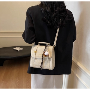 Detail of off-white leather handbag with vintage buckle and baseball charm accessory
