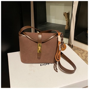 Detail view of brown faux suede bucket bag featuring golden twist lock and woven charm detail