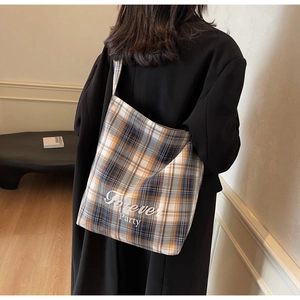 Sac fourre-tout en toile à carreaux porté par un mannequin dans un intérieur minimaliste