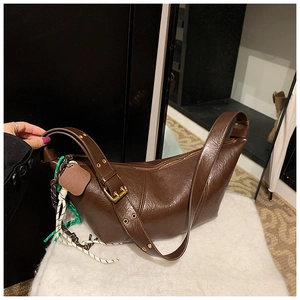 Detail of dark brown leather shoulder bag with wide adjustable strap and colorful woven charm