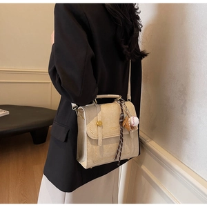 Close-up of beige crossbody bag with gold metal buckle and leather bag pendant