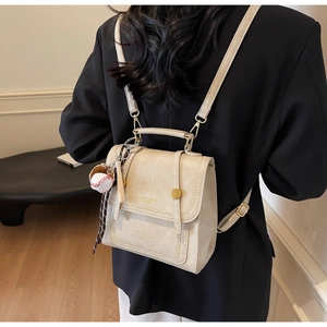 Model wearing a cream leather backpack with top handle and baseball keychain detail