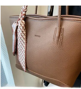Detail of dark brown lychee grain leather tote bag with embossed logo and silk scarf handle