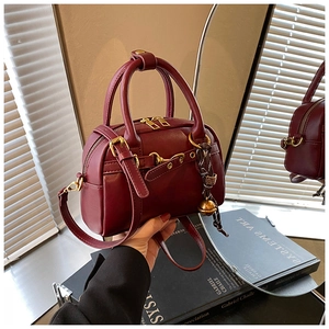 Détail du sac Boston bordeaux avec fermeture éclair dorée et breloque cloche décorative