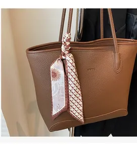 Close-up of brown pebbled leather tote bag with logo embossing and floral silk scarf