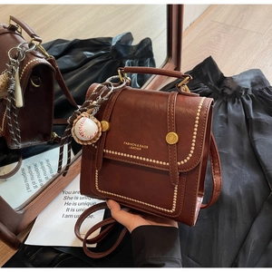 Detail of vintage brown leather bag with stitching and a mini baseball charm