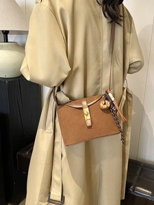 Retro brown frosted leather crossbody bucket bag with golden buckle on a khaki trench coat