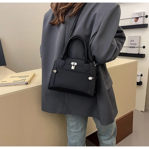 Close-up of black litchi pattern bag with silver padlock detail on a grey blazer