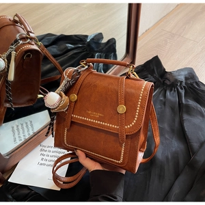 Detail of vintage brown faux leather bag with white stitching and baseball charm