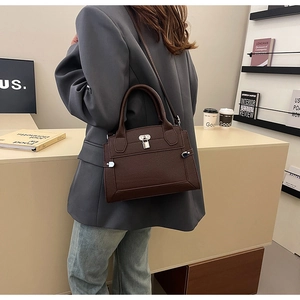 Detail of dark brown pebble leather tote with silver lock on model in grey blazer