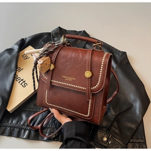 Detail of dark brown vintage faux leather backpack with gold rivets and cute charms