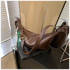 Detail of dark brown crescent bag with wide strap, metal eyelets and woven cord charm