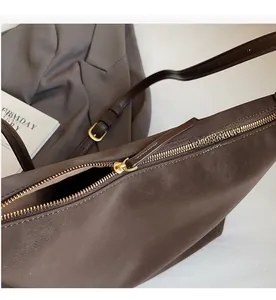Close-up of the smooth golden metal zipper detail on this brown suede leather tote bag