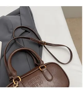 Macro detail of dark brown leather pillow bag with embossed ATN logo and gold hardware