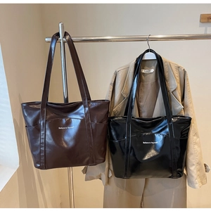 Detail of dark brown and black glossy PU leather tote bags with slogan and outer pocket