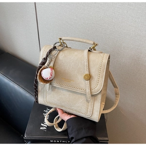 Close-up of cream faux leather bag with baseball charm and metallic buckle detail