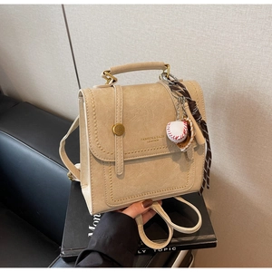 Detail of beige mini faux leather backpack with decorative scarf and baseball charm