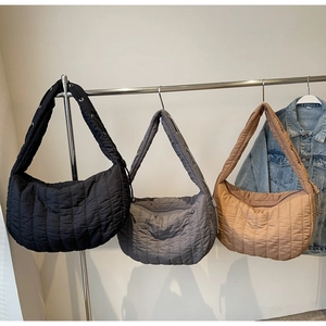 Close-up of quilted tote bags in black, grey and khaki colors hanging on a metal rack