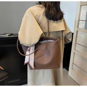 Detail of dark brown leather tote bag featuring a decorative sunflower silk scarf accessory