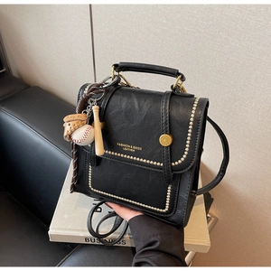Close-up of black retro bag with gold rivets, metal lock, and baseball charm detail