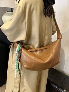 Brown leather half-moon shoulder bag with woven rope tassel on khaki trench coat