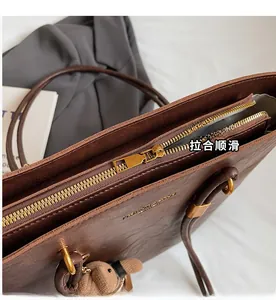 Détail d'une fermeture éclair fluide et texture cuir d'un sac cabas marron avec un pendentif